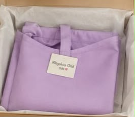 Prenda morada doblada con una etiqueta de marca tipo boutique, dentro de una caja de envío de cartón