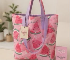 Un bolso de lona rosa con estampado de rodajas de sandía y asas moradas.