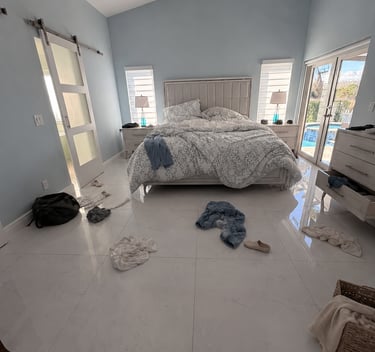 Messy modern master bedroom with clothes on marble tile flooring and light blue walls.