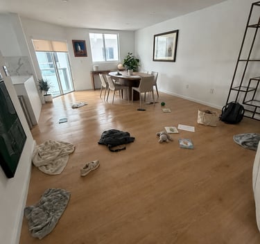 Messy modern living room with items scattered on light wood floors near a round dining table.