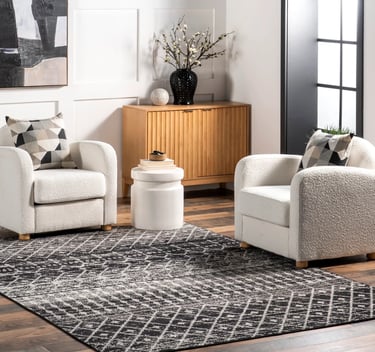 Modern living room with black and gray geometric area rug, white bouclé armchairs, and wooden sideboard.