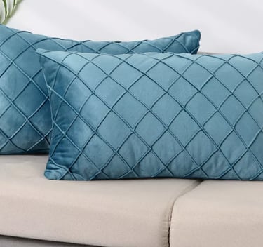 Pair of teal blue velvet lumbar throw pillows with a diamond quilted pattern on a gray sofa.