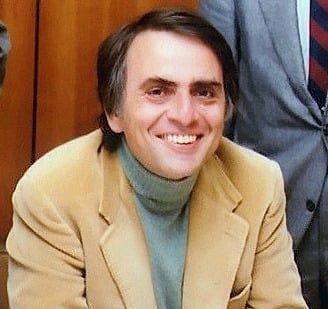 Carl Sagan in a suit and tie smiling at the camera