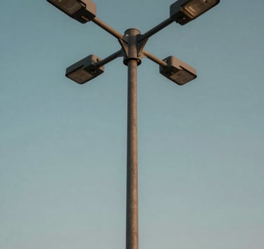 A low-angle professional shot of a modern street lighting pole against a clear sky in Riyadh, Middle Eastern / Gulf region, showing the sleek metal texture and robust construction, lighting in soft morning light with Dark Teal and Slate Blue hues.