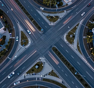 A high-angle aerial photograph of a complex road intersection in a modern International / Professional city, showing precise lane markings and infrastructure flow, captured with a professional focus and Steel Blue car light trails at twilight.