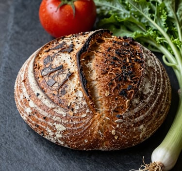 Professional high-contrast food photography of an artisanal sourdough loaf and fresh organic vegetables on a dark stone surface, captured in a North American / US farm-to-table restaurant kitchen.