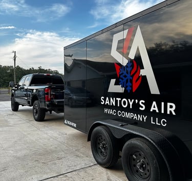 A black Santoy's Air HVAC company truck and service trailer parked on a driveway under a blue sky.