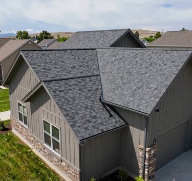 Wide angle shot of a suburban home in Colorado with a newly installed charcoal grey shingle roof, lush green lawn, bright daylight, North American / US.