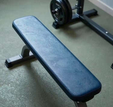An overhead view of a clean, organized workout space with a leather weight bench and polished weights, embodying a modern and results-oriented aesthetic. Tones of Steel Blue and Muted Sage dominate.