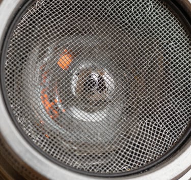 A close-up shot of a high-quality stainless steel chimney mesh filter, sparkling clean and reflecting soft orange ambient light.