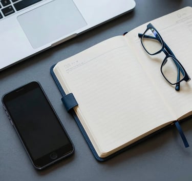 A top-down aesthetic shot of a organized desktop in a North American corporate setting. Features a modern smartphone, an open leather-bound planner, and a pair of professional glasses. The color palette includes muted blue and steel blue accents, conveying a sense of order and reliability.