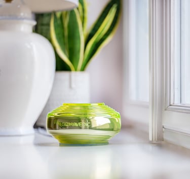 Somavedic green glass emf mitigation device on a bright windowsill next to a snake plant and ceramic lamp.