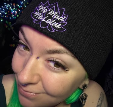 A smiling woman with green hair and a black beanie that says "no mud no lotus"