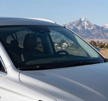 A pristine, newly replaced windshield on a modern luxury SUV, reflecting the clear blue sky and a distant mountain peak in a North American setting.