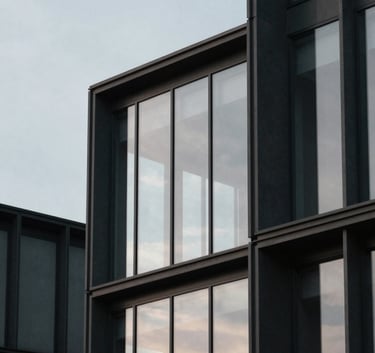 A minimalist wide shot of a contemporary building with glass facades reflecting a pale ash sky, framed with dark charcoal structural elements.