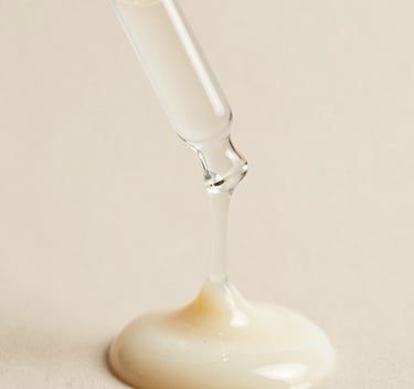 A macro photograph of a single laboratory glass dropper releasing a viscous, milky white serum into a soft neutral beige pool. Professional studio lighting with a clean, clinical feel in a modern North American / US setting. Focus on texture and premium science.