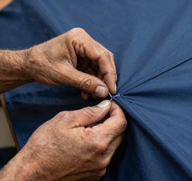 A close-up, high-detail photograph of a skilled artisan's hands in a workshop in Brazil, meticulously stitching a thick, navy blue weather-resistant canvas for an ombrelone.