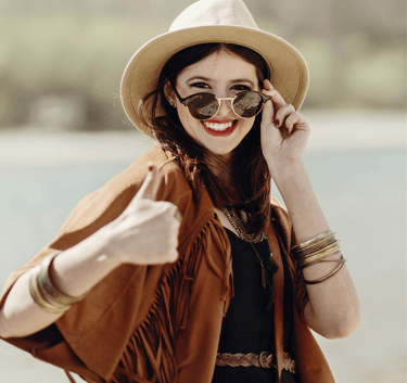 a woman in a hat and sunglasses is smiling and holding a cell phone