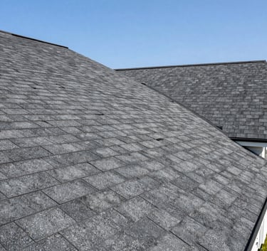 A wide, low-angle shot of a stunning newly finished residential roof with high-quality charcoal gray shingles on a North American suburban home. The composition is clean and strong under bright daylight.