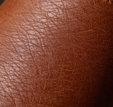 Extreme close-up macro photography of high-quality tanned leather, showing the natural grain and sophisticated texture in an earthy brown shade, representing the quality craftsmanship of a South American manufacturer.