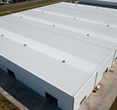 An aerial view of a massive North American warehouse featuring a pristine new white thermoplastic roof. The composition is clean and symmetric, emphasizing industrial scale and expert installation. Professional lighting highlights the smooth texture and durable quality.