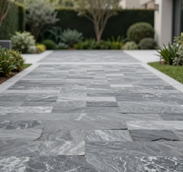 A wide-angle shot of a luxurious driveway paved with slate-textured stamped concrete in shades of #2E3A3A and #AEB9B4. The surrounding garden is impeccably landscaped, conveying professional craftsmanship and modern elegance.