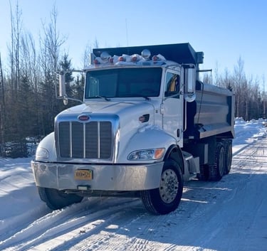 White Peterbilt dump truck parked on a snowy winter road with forest background.