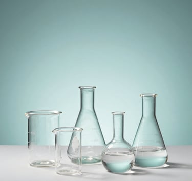 A minimalist studio photograph of elegant glass laboratory beakers and flasks arranged artistically on a white surface, with soft teal accents and professional lighting. Global Business / Professional.