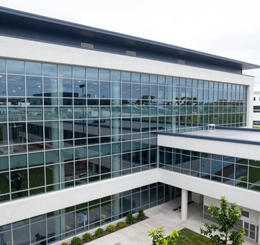 A high-angle professional photograph of a modern North American medical facility with glass walls and dark blue accents, bright natural lighting, and a clean minimalist aesthetic.