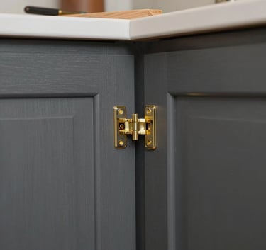 A close-up photograph of master woodworkers installing custom charcoal gray cabinetry with gold hinges in a North American / US - Los Angeles residence.
