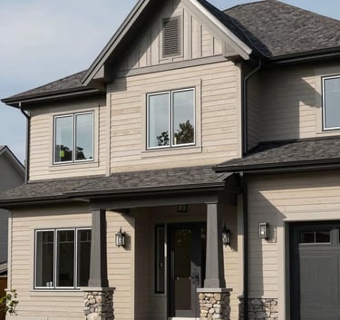 Exterior view of a luxury residential property in the Laurentides during a bright day. The house features high-end siding with a professional finish in shades of sand and gray. The architecture is typical of modern North American luxury homes.