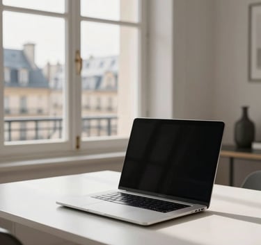 A sleek, minimalist home office in a French city with a view of historical architecture through the window, bright morning light, and a high-tech laptop on a white desk.