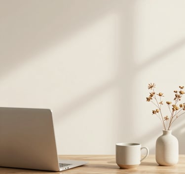 Minimalist and elegant home office setup featuring a laptop on a wooden desk, a ceramic cup, and a small vase with dried flowers. The color palette is warm cream #EADED4 and ivory #FAF7F5 with soft shadows.