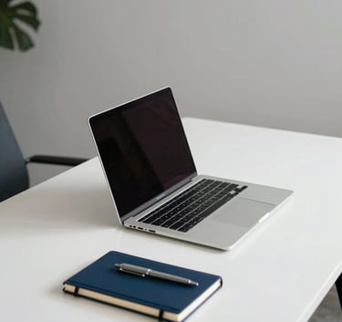 A clean, wide-angle shot of a minimalist North American office workspace with a white desk. A sleek metallic laptop is open on the desk, surrounded by a navy blue notebook and a silver pen. The lighting is soft and professional, highlighting a modern and efficient vibe.