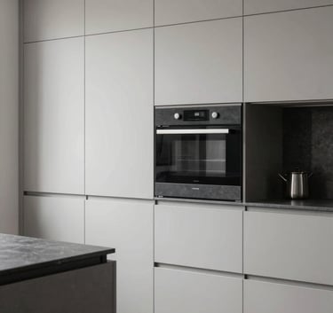 A high-end interior renovation scene showing a minimalist kitchen with light neutral grey cabinetry and charcoal dark slate grey hardware. Soft natural lighting emphasizes the modern craftsmanship and clean lines.