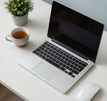 A minimalist home office setup viewed from above, featuring a laptop, a ceramic cup of tea, and a small green plant. The color scheme is dominated by soft blue-grey and soft off-white, creating a peaceful and focused atmosphere.