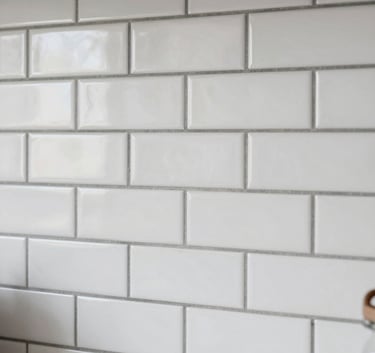 An elegant, clean-lined kitchen backsplash featuring white subway tiles in a herringbone pattern with contrasting dark slate grout. Sharp, precise photography with soft natural side lighting in a modern US residential setting.