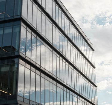A sleek, modern glass office building in Georgia during the day, reflecting a pearl white sky and soft sky blue highlights on its facade.