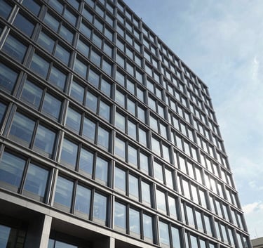 Wide-angle architectural photography of a high-end contemporary office building facade in a European / French city. Clean lines, steel and glass materials, shot during a bright day with a clear ice blue sky.