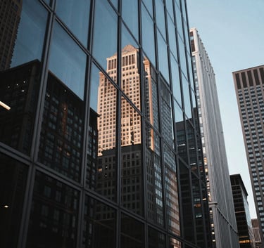 Wide-angle photograph of a sophisticated North American / US downtown skyline reflected in a polished glass window, evening light with midnight blue and silver grey hues.