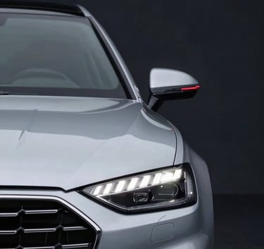 Close-up of a sleek, modern car front grille and headlight in a professional studio setting. The atmosphere is sophisticated and clean. Subtle red light (#A5002C) accents the curves of the vehicle against a deep dark background (#1A1A1A).