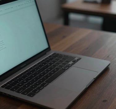 A close-up shot of a high-end laptop with a charcoal black finish on a dark wooden desk. A subtle modern teal glow emanates from the screen, illuminating a minimalist workspace in a sleek urban office environment.