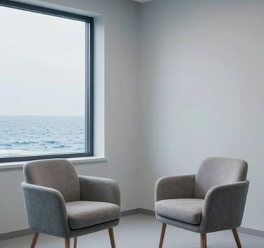 A clean, minimalist photography of a modern Western European / French consultation room with two comfortable chairs facing each other, large windows, ocean blue accents and pale frost grey walls, empathetic and professional lighting.