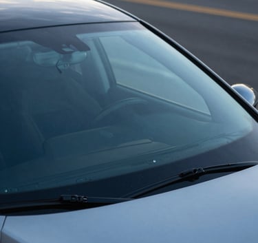Photography of a modern car parked on a quiet US street, showing the windshield reflecting a clear sky blue horizon, emphasizing safety and clarity, modern efficiency style.