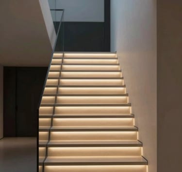 A luxury modern staircase at dusk with integrated LED lighting under the treads. The lighting is warm and inviting (#B28D69), contrasting beautifully with the deep shadows (#1A1A1A) and clean white walls (#FDFBF7).