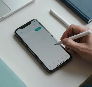 A top-down photograph of a professional workspace in the US, featuring a mobile device, a stylus, and a notebook on a clean light gray desk with soft teal and navy office stationery.