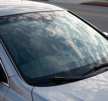 A high-end sedan parked on a North American / US suburban street during a bright morning. The focus is on a crystal-clear windshield reflecting the soft arctic white clouds and deep navy blue sky. Professional photography with sharp details and a clean composition.