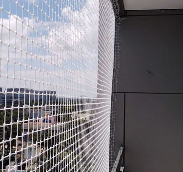 A clean, modern balcony with a professionally installed pigeon safety net. The lighting is soft and 