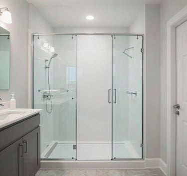A wide-angle shot of a bright, modern bathroom in a North American home featuring a large walk-in shower with clear glass, white surfaces, and light aqua accents.