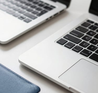 Macro photography of a sleek silver laptop on a white desk with a steel blue notebook nearby, representing digital efficiency and modern workflow.